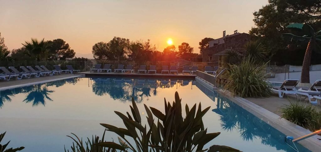 Piscine avec vue sur le coucher du soleil, chaises longues au bord de l'eau et végétation environnante.
